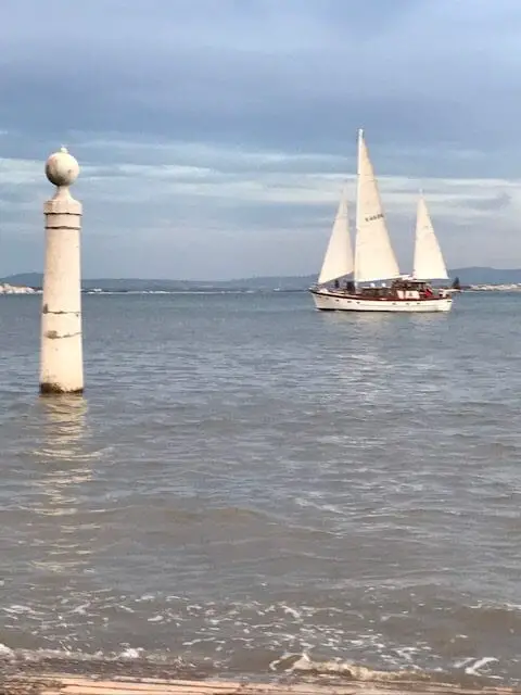Sailboat passing by the marble Cais das Colunas columns in the Tejo River in Lisbon.