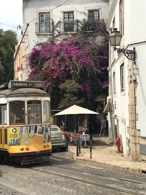 Yellow and white Tram 28 rounding the tight curves in Lisbon's medieval Alfama neighborhood.