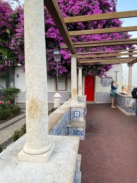 Blue and white tiled benches, wooden arbor, and bougainvillea flowers at Lisbon's Miradouro de Santa Luzia viewpoint