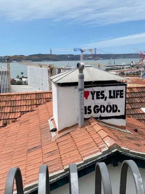"Yes, Life is Good" pasteup on a rooftop seen from Lisbon's Miradouro de Santa Catarina scenic viewpoint.
