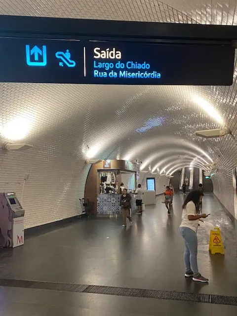 The sign says "SAida" Exit.  "Largo do Chiado" Chiado Square. "Rua de Misericordia."  Misericordia street.  Beyond that are escalators that go up to Lisbon's Chiado neighborhood
